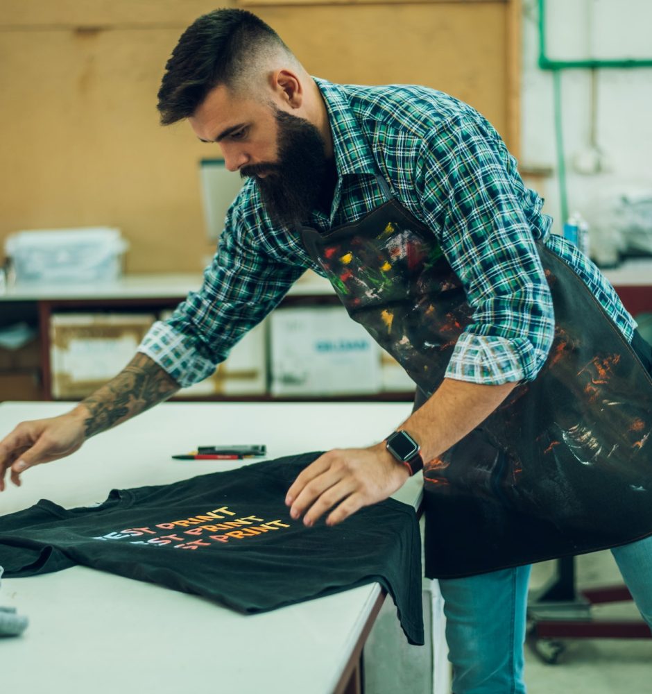 Male worker folding a fresh printed t shirt in a printing workshop